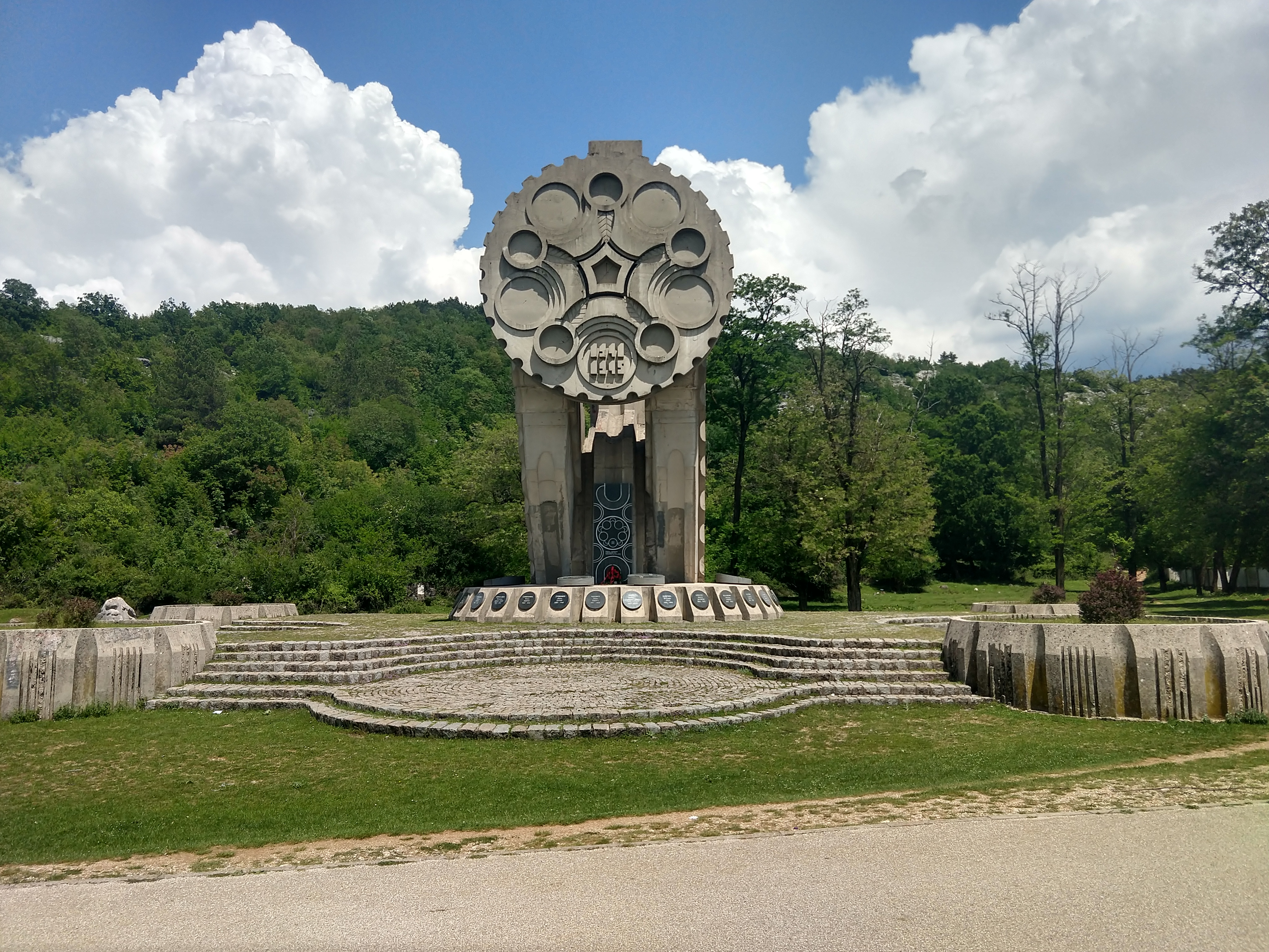 A monument in a green landscape beneath a bright, cloud-filled sky